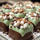 No-Bake Mint Chocolate Chip ClustersIngredients:- 1 cup semi-sweet chocolate chips- 1 cup white chocolate chips- 1 ½ cups miniature marshmallows- 1 cup chopped pecans- 1 teaspoon peppermint extract- ½ cup mini chocolate chips for garnish- Pinch of saltDirections:1. Begin by preparing a baking sheet lined with parchment paper. This will serve as the surface where you will place the clusters once formed, preventing them from sticking.2. In a medium microwave-safe bowl, combine the semi-sweet chocolate chips and white chocolate chips. Microwave the mixture on high in 30-second intervals. After each interval, remove the bowl and stir the chocolate. Continue this process until the chocolate is completely melted and smooth, which should take about 1 to 2 minutes in total.3. Once the chocolate is fully melted, add the peppermint extract and a pinch of salt to the chocolate mixture. Stir well to combine, ensuring that the extract is evenly distributed throughout the melted chocolate.4. In a large mixing bowl, combine the miniature marshmallows and chopped pecans. Pour the melted chocolate mixture over the marshmallows and pecans.5. Using a spatula, gently fold the mixture together until all the marshmallows and pecans are evenly coated with the chocolate. Be careful not to crush the marshmallows while mixing, as you want to maintain their shape.6. Using a tablespoon or a small cookie scoop, drop heaping spoonfuls of the mixture onto the prepared baking sheet. Make sure to leave some space between each cluster to allow for slight spreading as they set.7. Once all the mixture has been portioned out, sprinkle the mini chocolate chips over the top of each cluster for garnish. If necessary, press the mini chocolate chips lightly into the chocolate to help them adhere.8. Place the baking sheet in the refrigerator and chill for at least 1 hour, or until the clusters are set and firm to the touch.9. After the clusters have set, remove them from the refrigerator. Gently lift each cluster off the parchment paper and transfer them to an airtight container for storage. Keep the clusters in the refrigerator until you are ready to serve.