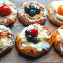 Danish Custard PastryFor Pastry SheetAll-purpose flour: 400 g or 3 cups + 1.5 tbspMilk (room temperature): 260 ml or 1 cup + 1.5 tbspButter: 180 g – 200 gSugar: 3 tablespoons (45 g)Salt: 1/2 teaspoon or 3 gActive dry yeast: 1 teaspoon or 3 gFor Vanilla Custard CreamMilk: 240 ml or 1 cupSugar: 50 g or 1/4 cupEgg: 1 gg + 1 egg yolkCorn Starch/ Plain Flour: 10g or 1 tbspSalt :1/8th tsp or 1 pinchVanilla Extract:2.5 ml or 1/2 tspButter: 15 g or 1 tbspFor the egg wash1 egg lightly beatenHow to make Danish PastryYou can make it in 4 simple stepsPrepare the pastry sheetShape the Danish PastryProof the Danish PastryBake the Danish PastryStep 1: Prepare the Pastry SheetThis is the most important part of the recipe. The pastry sheet is what gives this loaf its rich, layered, croissant-like texture.1. Make the DoughIn a large bowl, pour in the room temperature milk. Add sugar, salt, and yeast, and stir well until everything dissolves.Next, add the flour and mix until it comes together into a shaggy dough.Now, knead gently for about 1 minute, just until you get a smooth, soft dough without lumps or dry spots. You don’t need to over-knead or test for the windowpane stage — this dough is meant to be easy!This dough isn’t very sticky, so you’ll find it quite manageable.Roll and form it into a log shape.Divide and Shape the Dough BallsDivide it into 12 equal pieces. Roll each piece into a smooth ball.Cover the dough balls with a damp kitchen towel and let them rest for around 15 minutes.This short resting time relaxes the gluten, making it easier to roll them out later without the dough shrinking back.3. Flatten and Layer with ButterAfter the resting time, take one dough ball and roll it out into a disc about 16–18 cm in diameter and about 2 mm thick.Spread about 1 tablespoon of butter evenly on the surface of the disc.Then place it on a plastic film or parchment sheet.Once all discs are stacked and buttered, cover the pile with cling film.I watched the clock to see how long it would take me to make this pastry stack. And the layering process took only 34 minutes.Freeze the Dough StackSince the butter will be soft, it’s important to firm it up before shaping.Place the stacked dough in the freezer for 30–35 minutes until the butter becomes slightly firm and pliable.This step ensures that when you roll out the dough later, the butter stays inside as neat layers instead of melting out.Step 2: Shape the Danish PastryAfter the stacked dough has chilled and the butter is firm, take it out from the freezer.Roll the stack into a rectangular sheet about 1/4 cm thick (12 x 16 inch rectangle). Trim off the edges to form straight ends.This Danish Custard Pastry recipe is sufficient to make 12 medium sized delicious pastries.Using a knife or pizza cutter, cut the dough into squares of 4 inch size.Now, fold corners slightly(as in video) towards the center.Step 3: Proof the DoughCover the shaped Pastries with a plastic wrap and let it proof for around 1 hour, or until it rise a little and looks puffy. We don’t want them proof well and get a bread-like texture.The time can vary depending on your room temperature,(in warm temperature it will rise fast and in colder environment it may take slightly longer) so keep an eye on the dough sheet rather than the clock.Step 4: Bake the Danish Custard PastryOnce the Pastry square has risen, brush the top with egg wash (lightly beat one egg ). This helps create that beautiful golden-brown shine after baking.Prick the center of each pastry square with a fork to prevent it from puffing up while baking.Fill the center of each pastry with custard cream and then with some fruit jam or fresh berries or fruits(optional).Bake the Danish Pastry in a preheated oven at 375°F (190°C) for about 35 minutes.You’ll know it’s done when the top is deep golden brown.After baking, remove the pastries from the oven and transfer it to a wire rack to cool completely.They have beautifully flaky crust and they are soft and fluffy inside and if filled with creamy vanilla custard with sweet and sour strawberry jam in the center.These Danish Custard pastries are best to serve while they are just cooled down.How to make Vanilla Custard CreamInto a small bowl, add the sugar, salt, corn starch, egg and egg yolk.Mix and combine until you get a smooth, lump-free paste.Pour in a little hot milk slowly to lighten the mixture while stirring continuously to avoid scrambling the eggs.Then pour this mixture back into the saucepan with the remaining milk and cook over medium heat.Keep whisking until the custard starts to thicken and large bubbles form.Remove from heat and add vanilla extract and butter.Whisk again until you get a smooth and glossy cream.Let it cool before using.