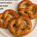 Soft PretzelIngredients• 3 cups all-purpose flour• 1 cup warm water• 2¼ tsp sugar• 1 tsp saltInstructions1. Activate yeast:Combine warm water, sugar, and yeast. Let it sit for 10 minutes until foamy.2. Make the dough:Add flour and salt; knead until smooth and elastic. Let it rise for 1 hour.3. Shape pretzels:Divide dough into 3 pieces. Roll into long ropes and twist into the classic pretzel shape.4. Boil in baking soda water (optional):Boil each pretzel for 30 seconds to get the chewy texture.5. Bake:Sprinkle coarse salt and bake at 200°C (400°F) for 12–15 minutes until golden brown